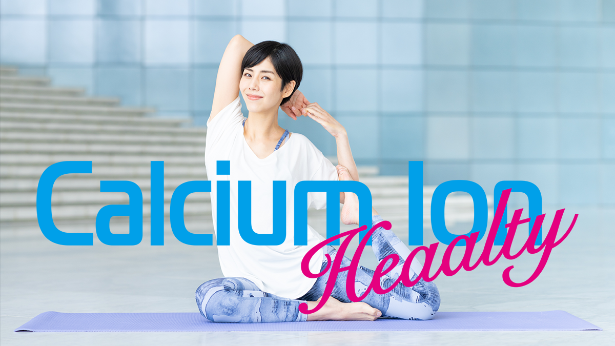 タイトル「Calsiumu Ion ヘルシー」の背後に、屋外のガラス張りの我部のあるスタジオで女性がヨガのポーズをとっているをしているシーンの画像