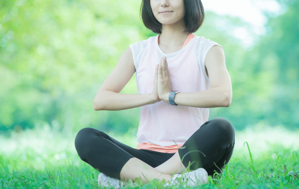 公園の芝生の上で、禅のポーズをする若い女性の写真
