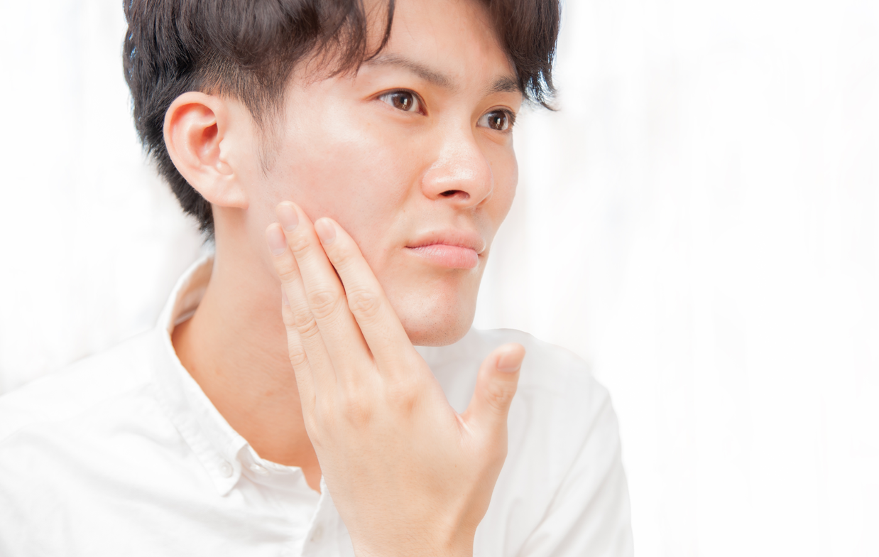 顔の肌を手でたあいかめる若い男性の画像
