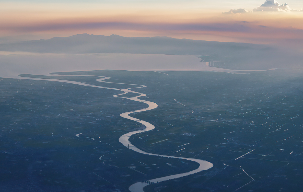 朝焼けの眼下の平野を川が蛇行する空撮写真
