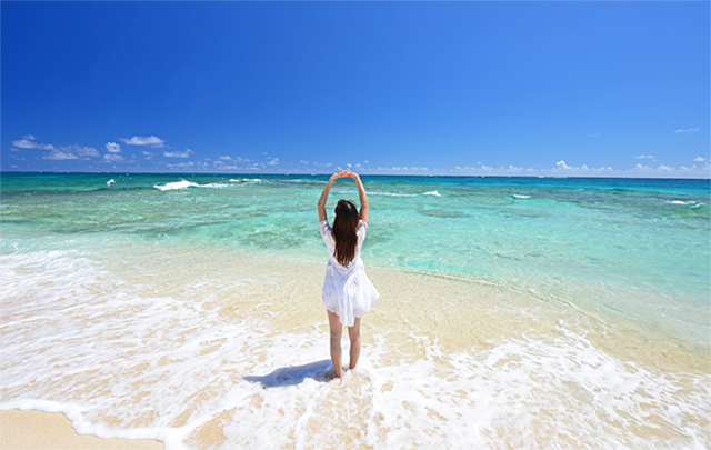 波が押したり引いたりする波打際に少女がたたずむ写真