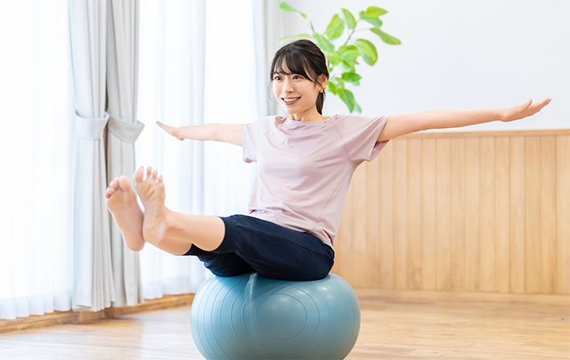 バランスボールに乗って水平バランスをとっている若い女性の画像