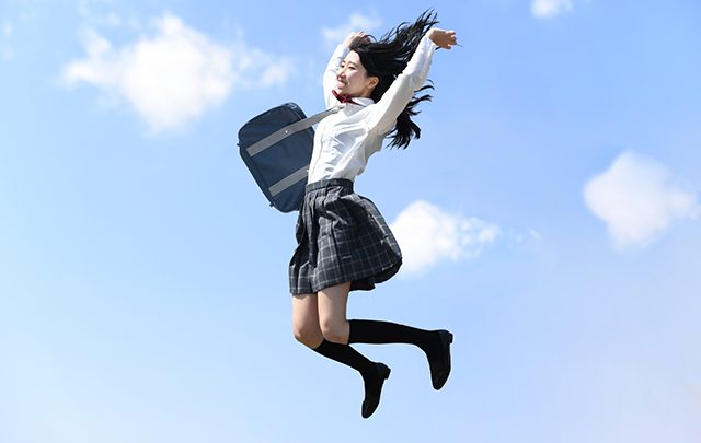 青空を背景にジャンプする女子学生の画像