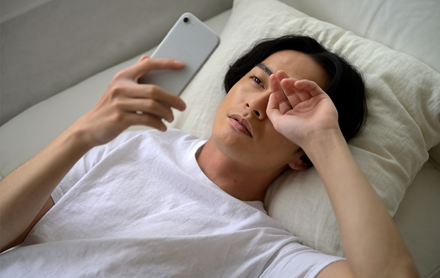 深い眠りを阻害する睡眠前のスマホを操作する若い男性の画像