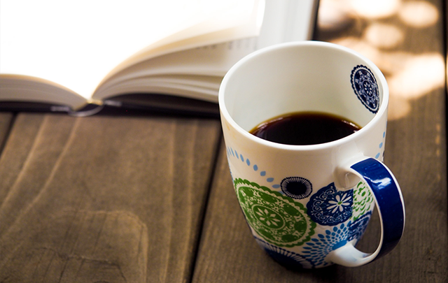 飲みかけのコーヒーと読みかけの本が拡げ得られている画像