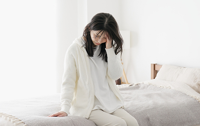 ホルモンバランスを崩して憂うつにベッドから起き上がる女性の画像