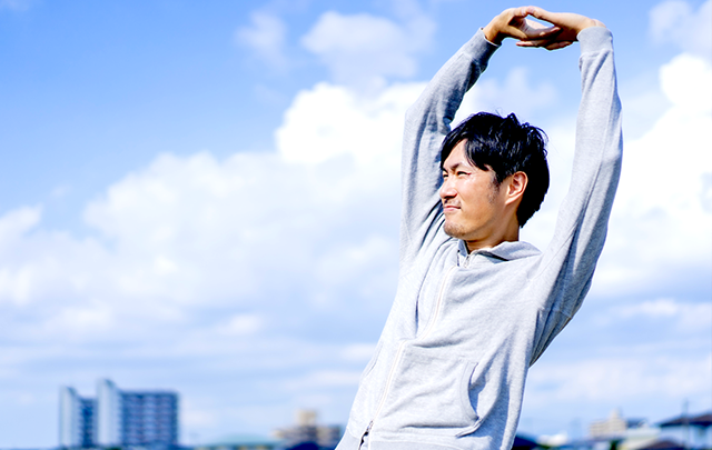 青空の下で背伸びをしている男性の画像