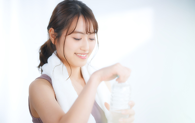 首にタオルをかけて水を飲む女性の画像