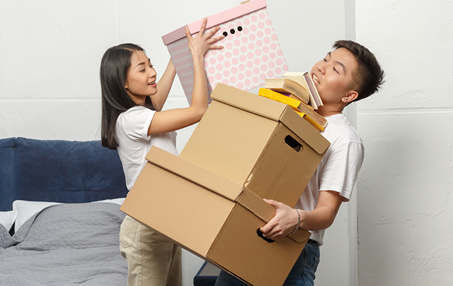 積み重なる荷物の上にさらに女性同僚が荷物を載せようとしている画像