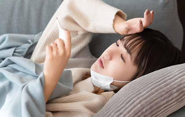 風邪で寝込み体温計で熱を測る女性の画像