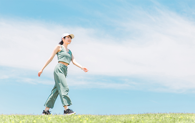 青空のもと堤防を背筋を伸ばして歩く若い女性の画像