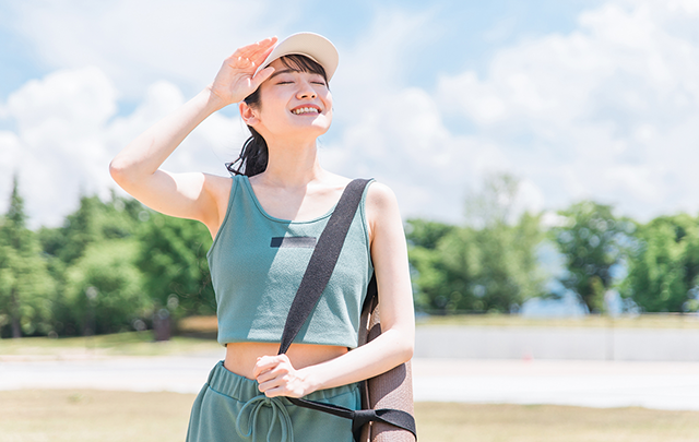 太陽をまぶしそうに見上げる散歩中の女性の画像