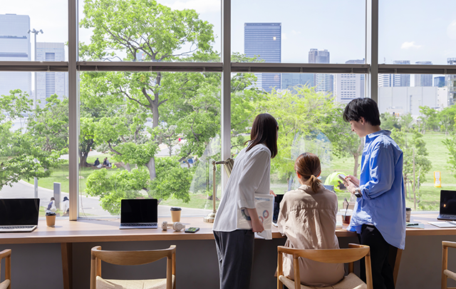 大きな窓際で仕事をする3人の男女オフィスワーカーの画像