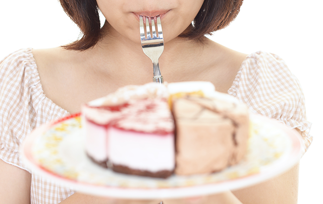 伊ケーキザラにのっているいくつかのケーキを抱えてフォークを国に加えている女性の画像