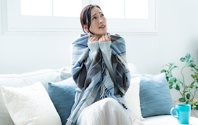 部屋の中央のソファに座って寒さに凍える女性の×増