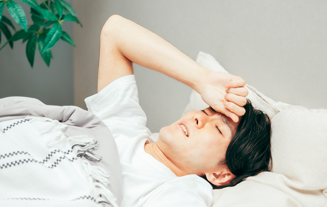 ベッドの中で額を抑える若い男性の画像