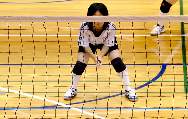 ネット前のコートで守るバレーボール女子選手の画像