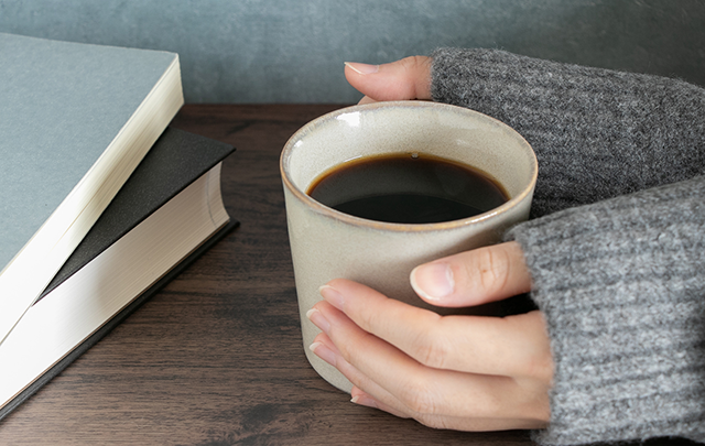 コーヒーカップを両手で温めている女性の手のアップ画像