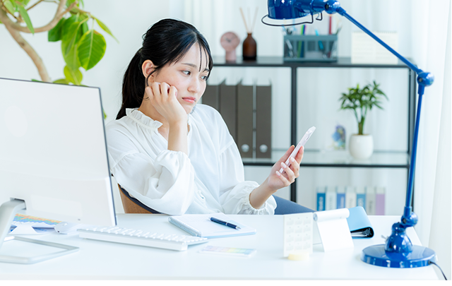 オフィスでパソコンやスマホを使って仕事をしている女性の画像
