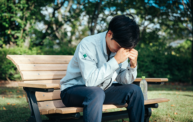 公園のベンチに座って気分が落ち込みかがむ若い男性の画像