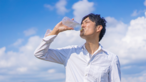 青空の下で飲料を飲む壮健な男性のイメージ