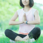公園の芝生の上で、禅のポーズをする若い女性の写真
