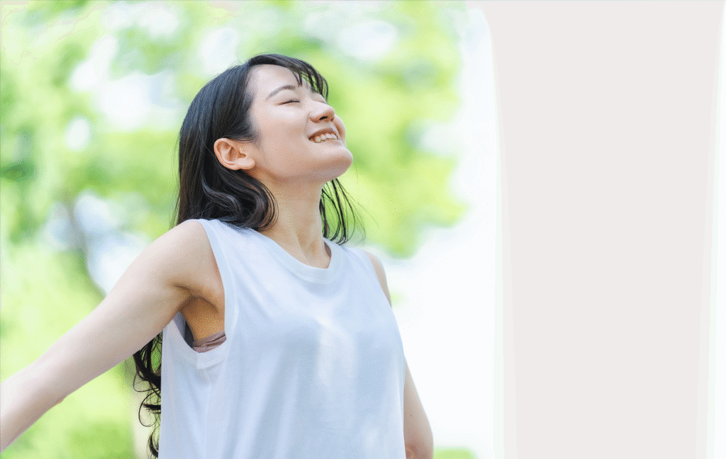 新緑の木下で、大きく手を広げて呼吸する若い女性の写真