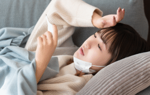 風邪で寝込み体温計で熱を測る女性の画像
