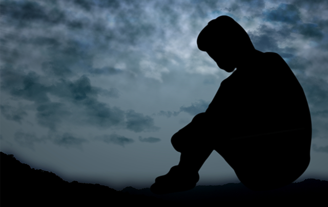 暗い曇りっ空を背景に堤防の土手でうずくまる男性の画像
