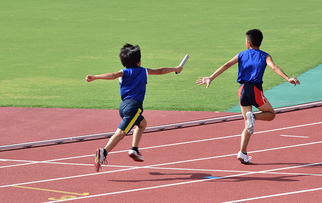 先行ランナーに走り切ったランナーがバトンパスしようと手を伸ばししてている画像