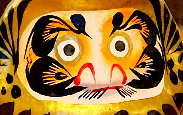 不屈の精神を表す金色ダルマの顔のアップ画像