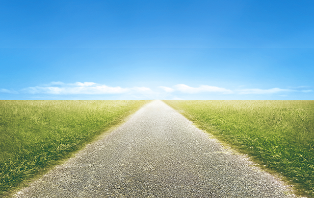 青空のもとの草原の中央にまっすぐな一本道の画像