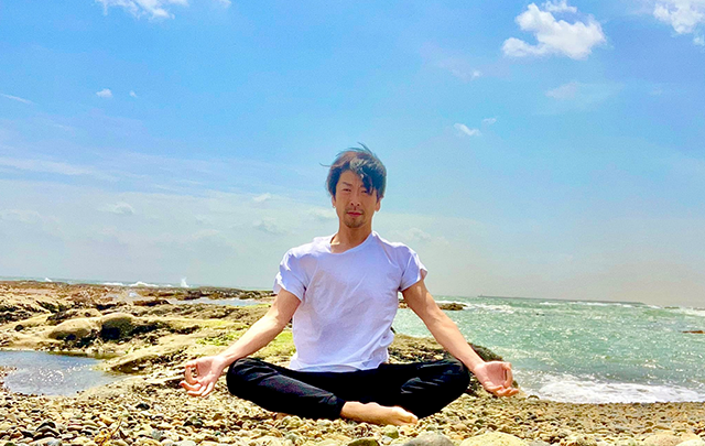 お青空の海岸のそばで座禅を組む男性の画像