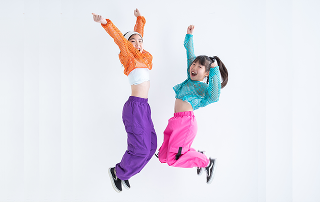 ストリートダンスでジャンプする蛍光色カラーのカジュアルな服を着たふたりの少女の画像