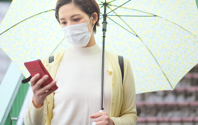 雨傘をさして、スマホをM見ながら会うr区若い女性の画像