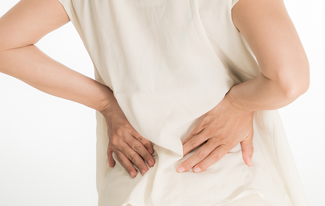 背骨のまがりからくる疲れで腰を抑える女性の背中の画像