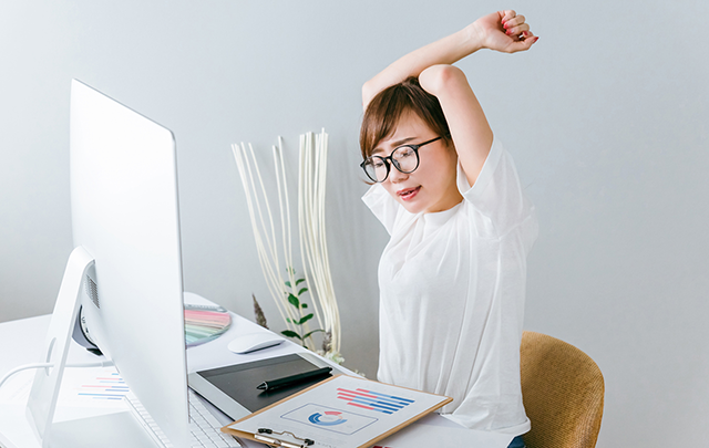 仕事をしながらストレッチをしているながらワークをする女性の画像
