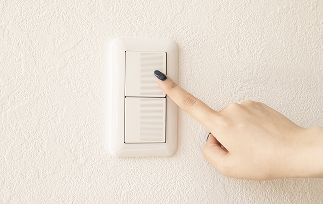 部屋の明かりのスイッチを押す女性の手の画像