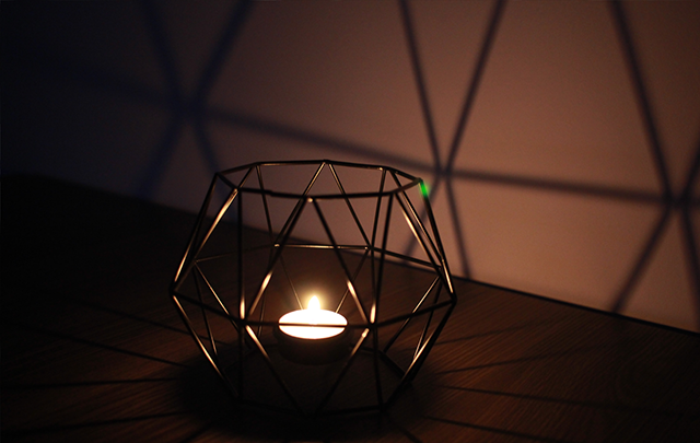 暗がりを照らす寝室の壁際の竹かごに置かれたキャンドルの画像