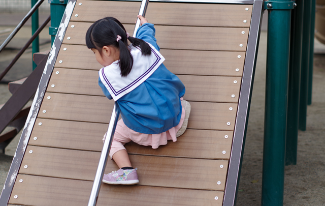 公園の遊具の傾斜に手すりを両手で登る女児の画像