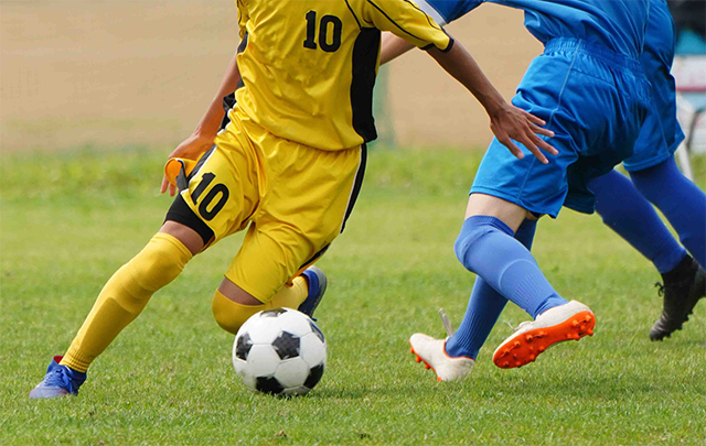 サッカーで２人の選手がボールを競り合っているところの画像