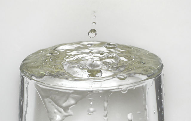 コップにたっぷりの水が注がれて溢れ出している画像