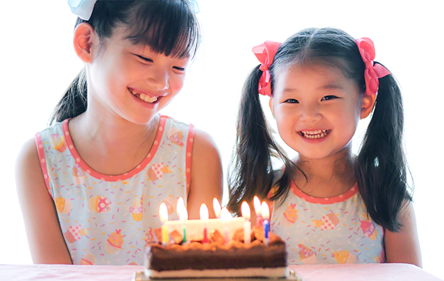 小学生の姉妹が誕生日のケーキを前に笑顔の画像