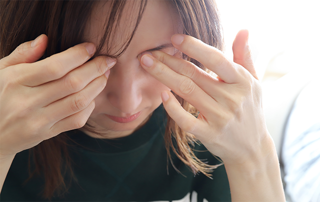 俯いて目をおさえる若い女性の画像