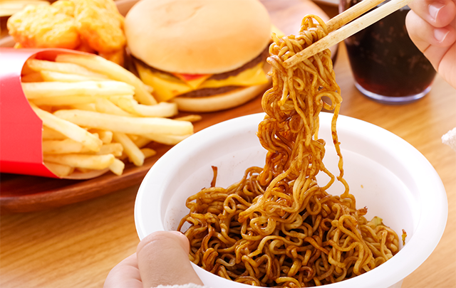 カップラーメンやファストフードなどのをテーブルにひりげ食事している画像