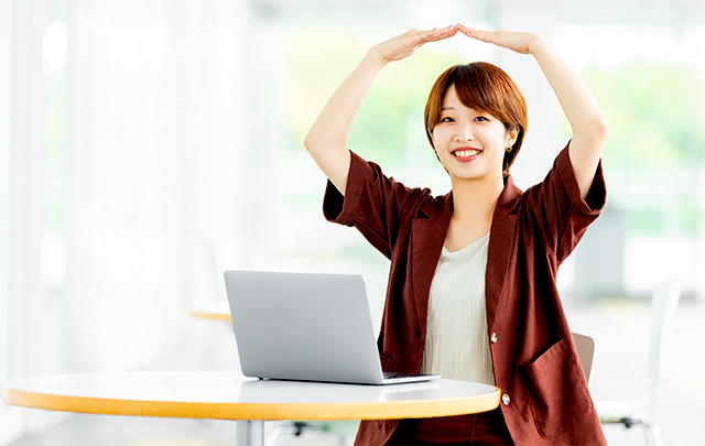 離れた同僚に頭上で◎を作ってサインを送る女子社員の画像