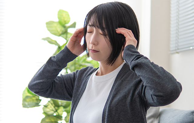 気圧の低下で頭痛になり頭を抱える女性の画像