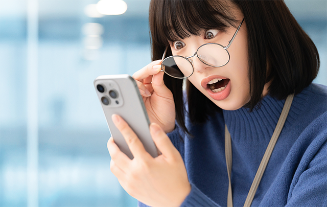オフィスでスマホのニュースを見て驚く若い女性のビジネスピープルの画像