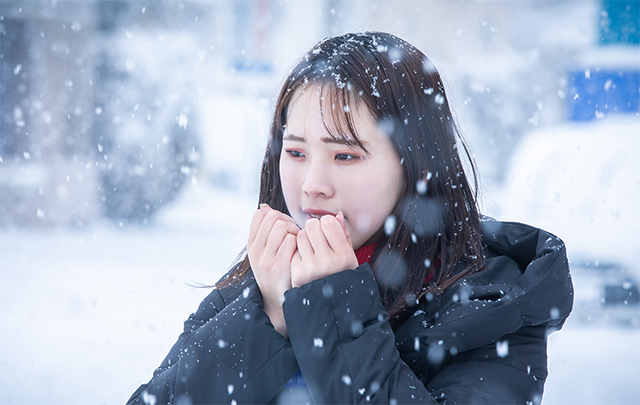 雪の降る中、両手を温める女子学生の画像