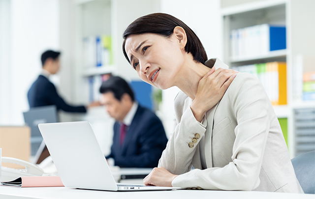 オフィスのデスクで片手で肩をさする若いOLの画像